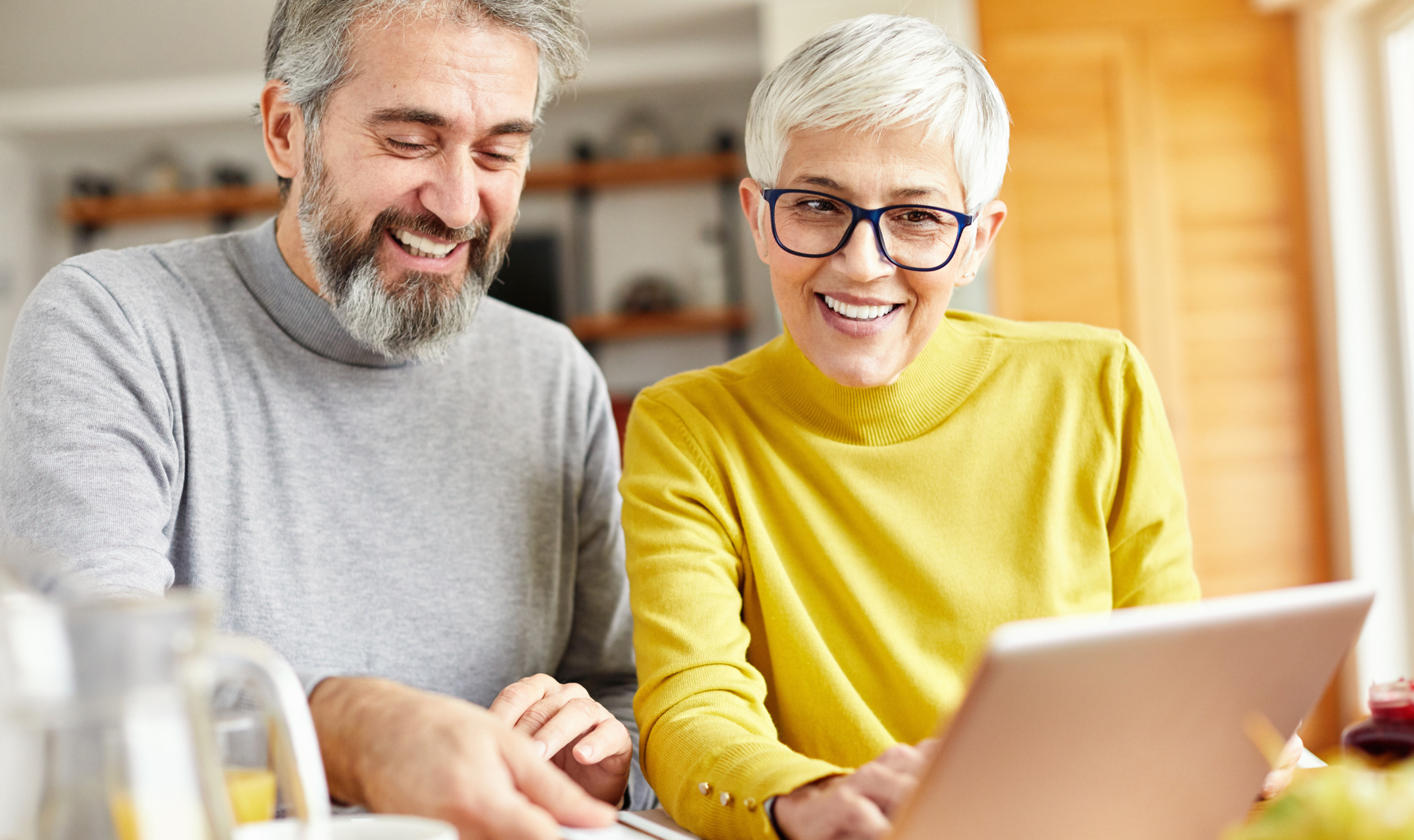 Smiling man in grey and smiling woman in yellow looking at a computer